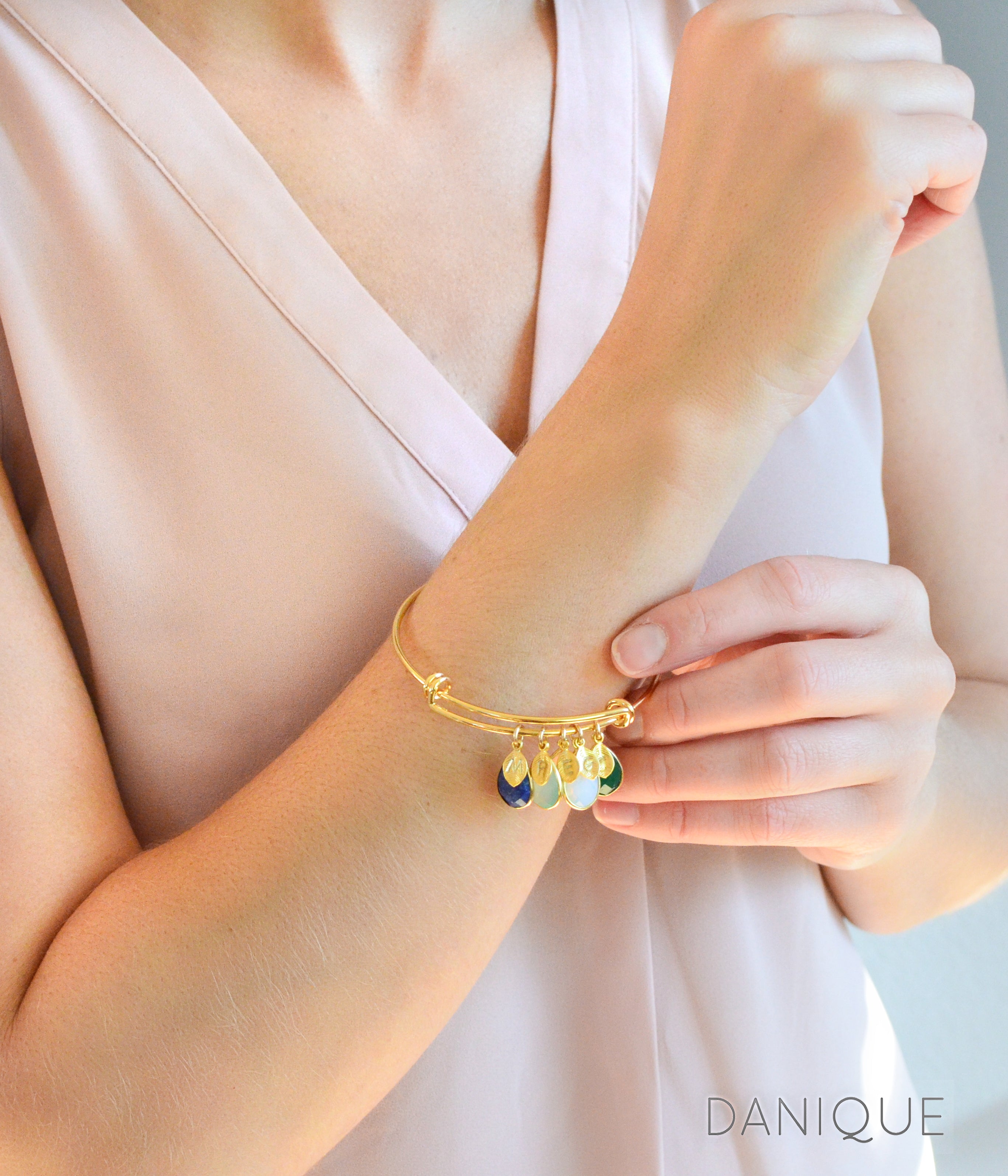 Model in cream top is wearing a single gold bangle bracelet with stamped leaf charms and lapis, aqua chalcedony, opalite and green onyx birthstones.