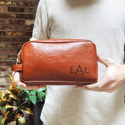 Personalized men’s leather toiletry bag engraved with initials, shown in cinnamon brown. Ideal as a groomsmen gift, birthday present, or travel shaving kit accessory.