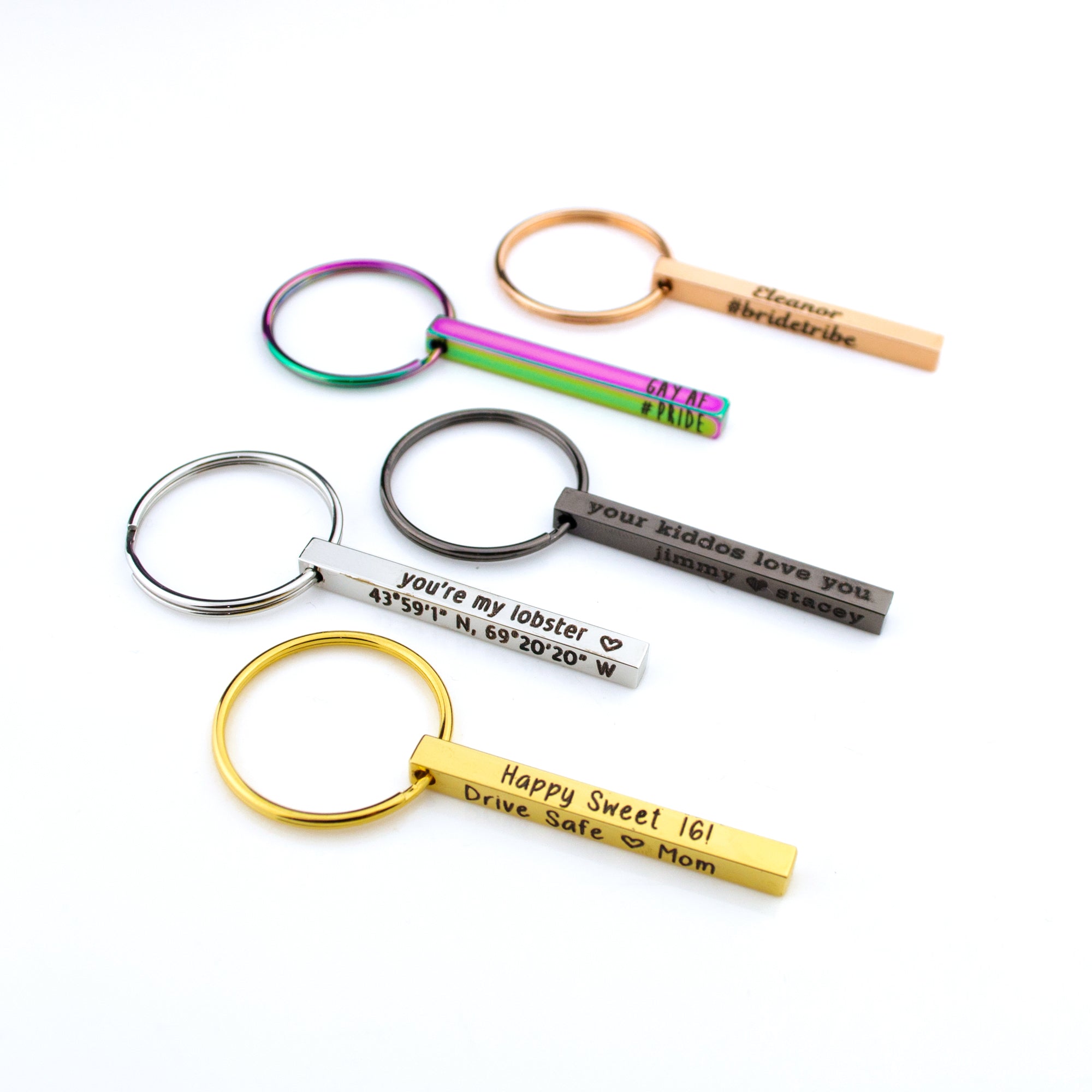 Compact 3D bar keychains in silver, gold, rose gold, black, and rainbow finishes arranged on a white background, each bar engraved with custom names, dates, or GPS coordinates. The dainty mini bar keychain design (40×4 mm) shows slimmer proportions that fit pockets and purses, while the matching spring key rings highlight durability. Ideal personalized keychain gifts for anniversaries, new drivers, graduates, dads, and groomsmen.