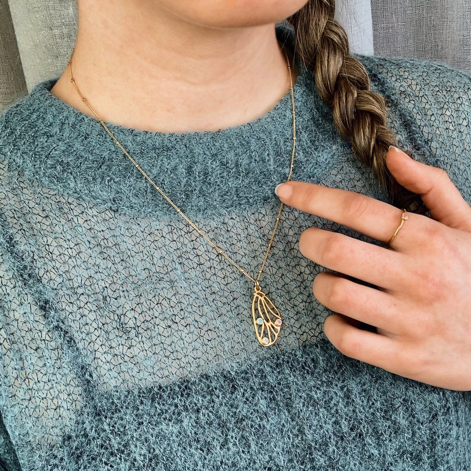 Model is wearing a gold plated butterfly wing pendant with aqua chalcedony, pink chalcedony and moonstone birthstones on a satellite style chain. 