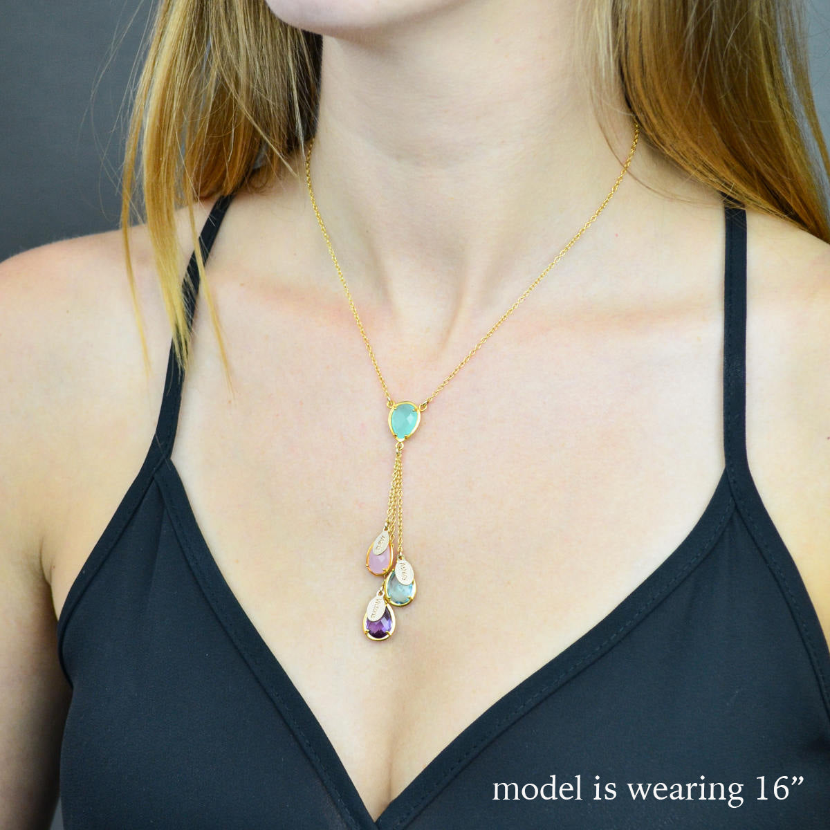 Model is wearing a gold lariat mother's necklace with  aqua chalcedony double loop teardrop birthstone, three hanging birthstones with full names engraved on name tags. Stones include: pinky chalcedony, blue topaz and purple amethyst
