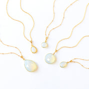 Dainty opalite pendant necklace displayed on white satin background in gold, silver, and rose gold. October birthstone jewelry featuring luminous opalite gemstone — a meaningful jewelry gift for her. Perfect for birthdays, anniversaries, Christmas, or bridesmaid gifts. Minimalist opal necklace handcrafted in the USA by Danique Jewelry, available in multiple shapes and finishes for everyday wear or special occasions.