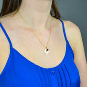 A person in a blue shirt wears a gold paw print disc necklace with a red ruby July birthstone. 16mm paw print pendant, custom birthstone necklace, pet lover gift, sterling silver disc necklace, gold-filled jewelry, rose gold-filled necklace, personalized pet accessory, engraved pet keepsake, unique pet memorial, custom double-sided engraving, dainty charm