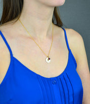A person in a blue shirt wears a gold paw print disc necklace with a red ruby July birthstone. 16mm paw print pendant, custom birthstone necklace, pet lover gift, sterling silver disc necklace, gold-filled jewelry, rose gold-filled necklace, personalized pet accessory, engraved pet keepsake, unique pet memorial, custom double-sided engraving, dainty charm