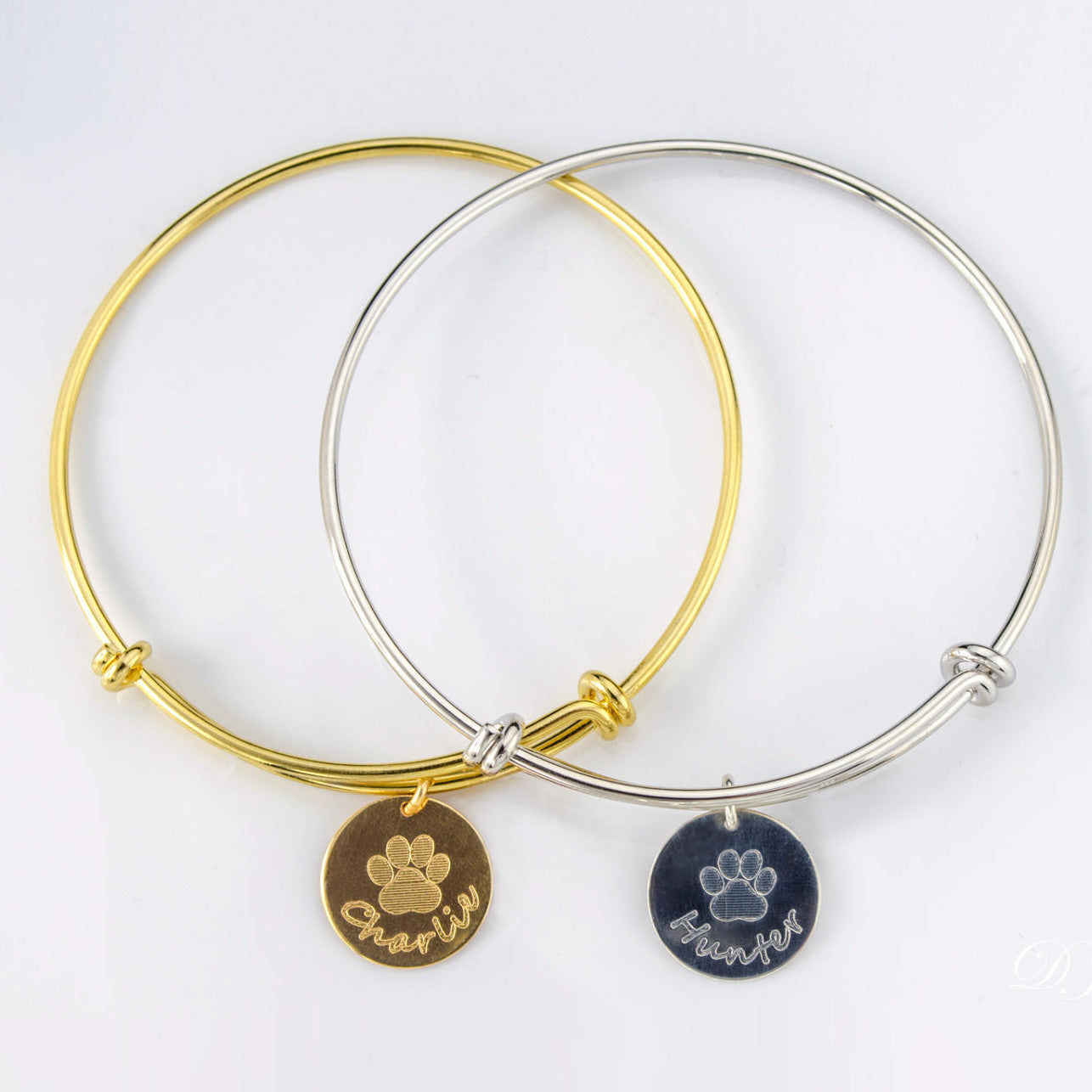 One gold bangle bracelet with stock paw print and name engraved on the front. One silver bangle disc bracelet with stock paw print and name engraved on the front.