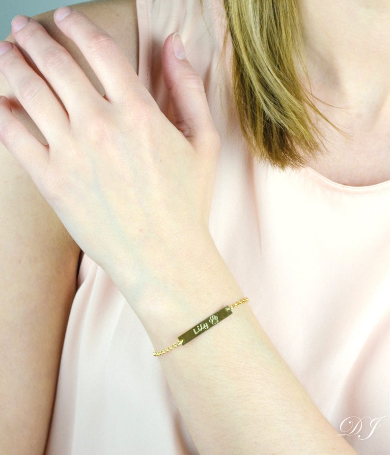 Model is wearing this versatile and minimal bar bracelet in gold filled with script writing and stock paw print 