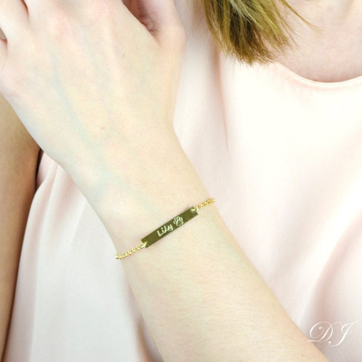 Model is wearing this versatile and minimal bar bracelet in gold filled with script writing and stock paw print 