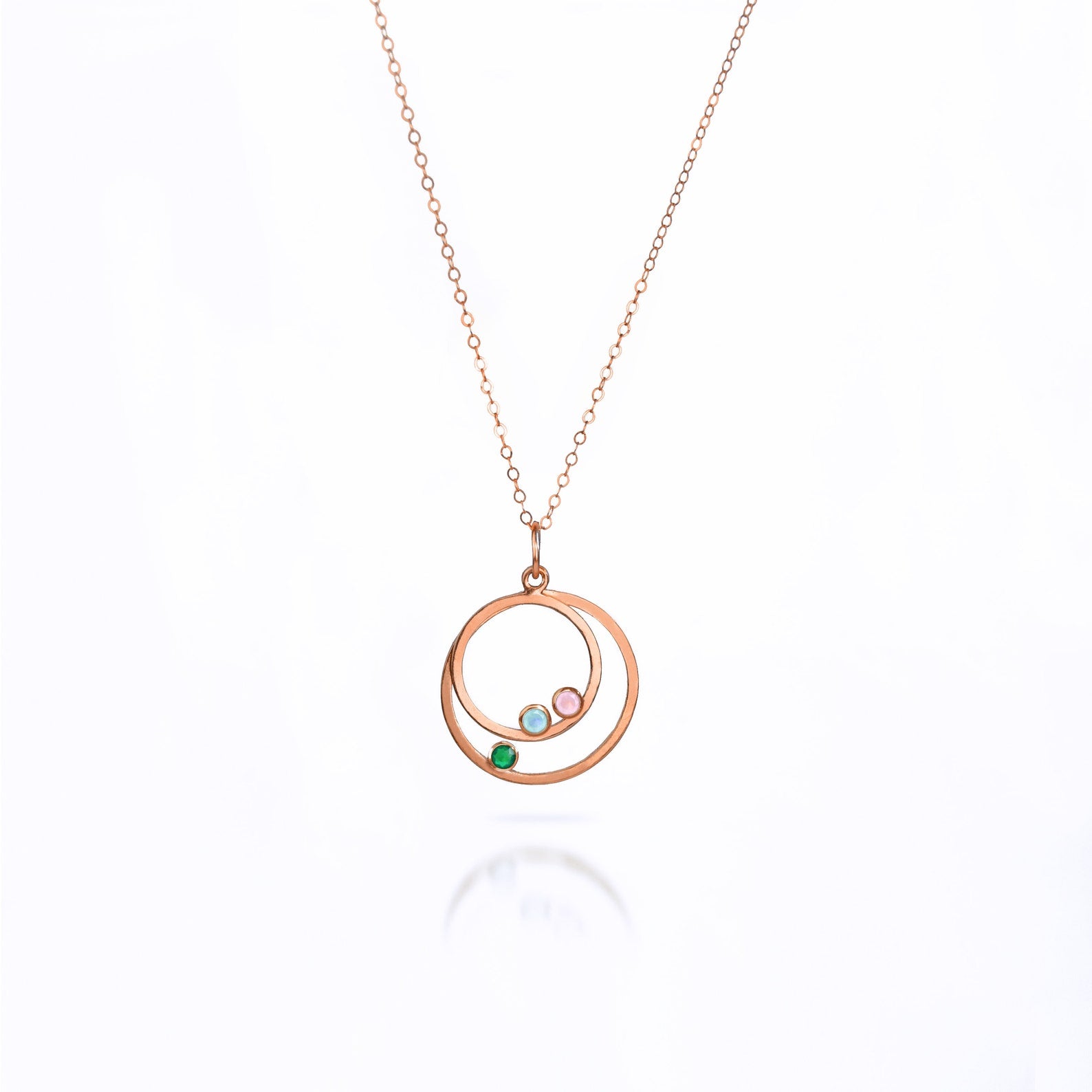 Single orbital necklace in rose gold filled cable chain with two orbits small ring with aqua chalcedony and pink chalcedony and larger ring with green onyx birthstone. 