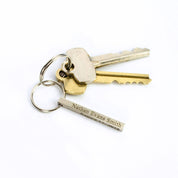 Minimal silver small 3D bar keychain attached to a set of keys on a bright white background. The compact 40×4 mm bar shows fine laser lettering and smooth corners, designed for pockets without bulk. Customize this personalized keychain with monogram initials, roman numerals, or latitude and longitude to create a meaningful everyday accessory for him or her.