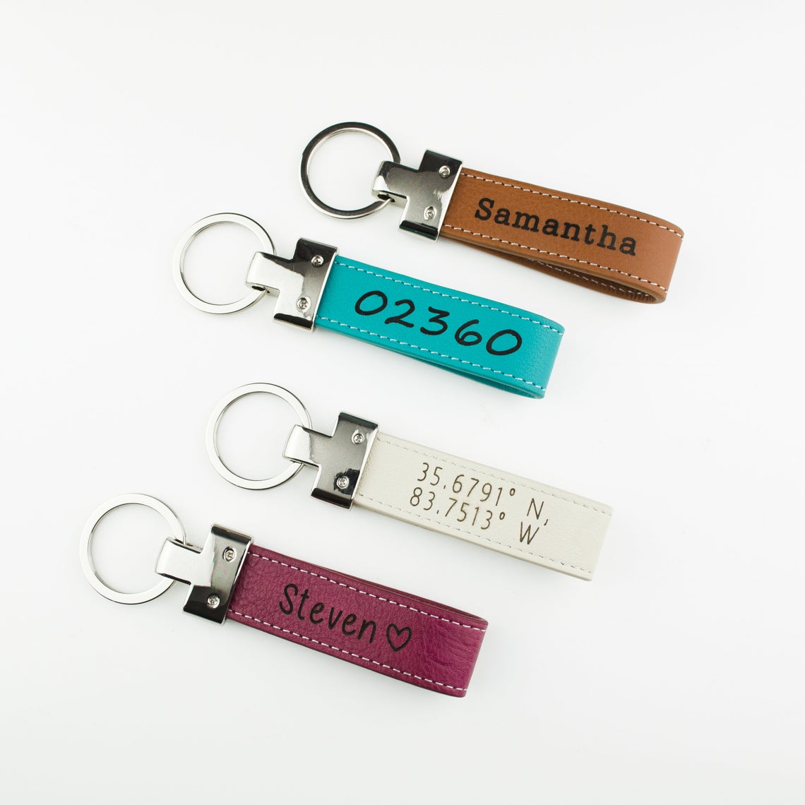 Four Personalized Engraved Genuine Leather Loop Keychains with stainless steel keychain loops. Brown Leather Keychain with custom engraved name, Turquoise Leather Loop Keychain with zipcode or custom numbers engraved, White Leather Loop Keychain with custom engraved coordinates, raspberry pink leather loop keychain engraved with name and a heart