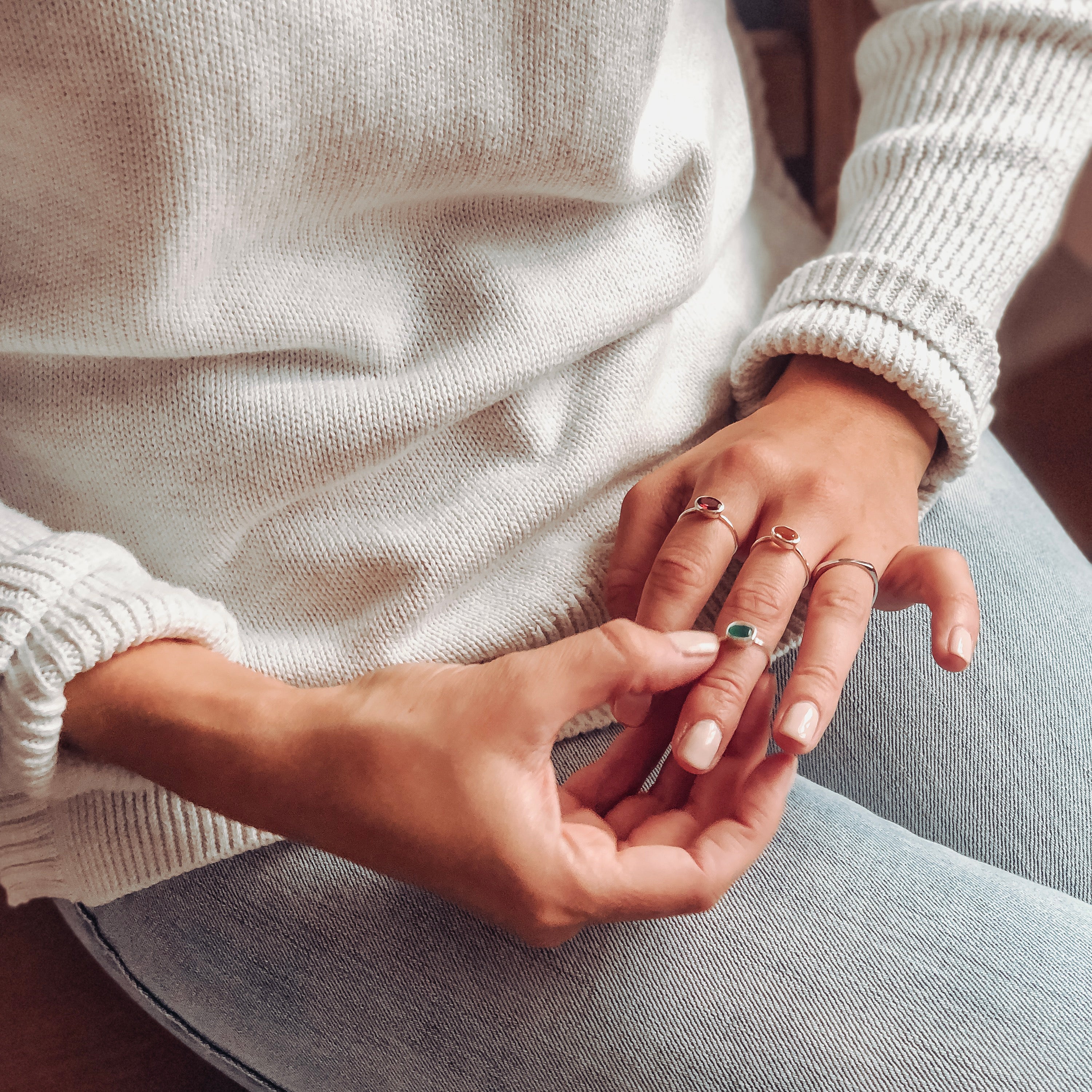 Model wearing three rings. One silver on the index finger with the ruby gemstone, two sterling silver rings on middle finger with garnet and green onyx stones. 