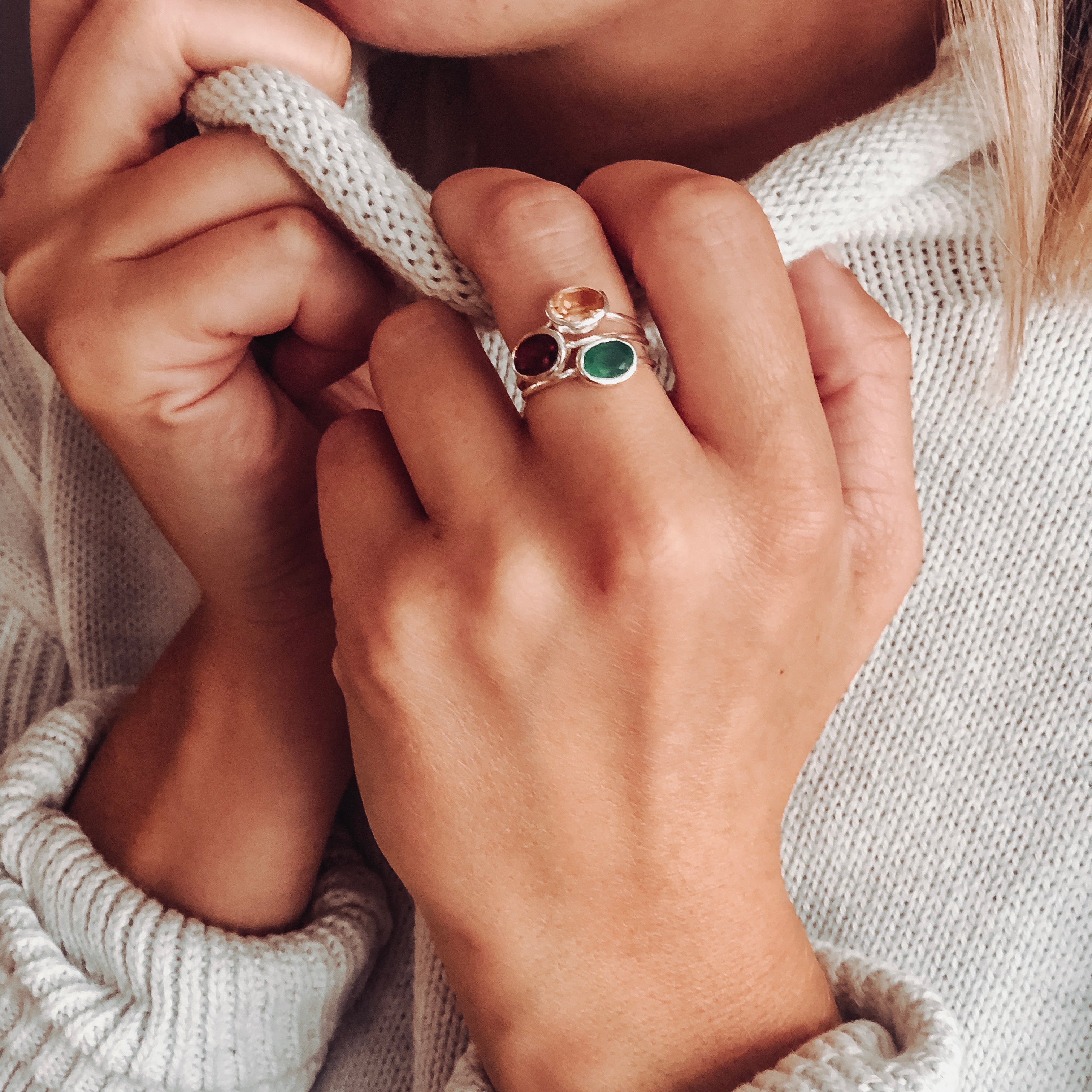 Model in white sweater is stylishly stacking three sterling silver oval rings including citrine, garnet, and green onyx