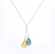 Minimalist lariat birthstone necklace in bright sterling silver showing two faceted teardrops—sky blue and golden yellow—set in bezel frames. Modern, elegant support-Ukraine pendant designed for everyday wear or layered looks. Adjustable chain with delicate profile makes a thoughtful solidarity gift for friends and family. Keywords: necklace ukraine, teardrop birthstone, sterling silver necklace, blue and yellow pendant, dainty layered necklace.