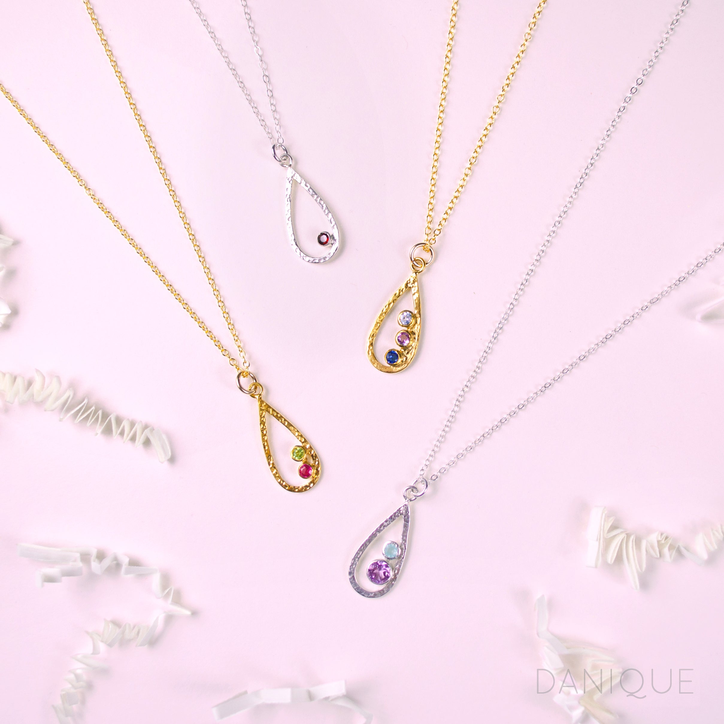 Two sterling silver teardrop pendant frame necklaces, one featuring a single garnet gemstone, one in our mother and child stone style with a 5mm purple amethyst and 3mm aqua chalcedony birthstones. Two gold filled open teardrop pendant necklaces one with peridot and ruby birthstones and one with blue topaz, purple amethyst and kyanite birthstones. 