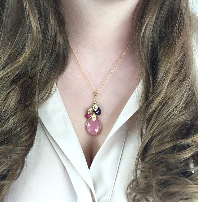 Model in white top is wearing a gold filled mothers necklace with large pink chalcedony birthstone and ruby and onyx kids birthstones with hand stamped leaf charms