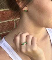 A person wears a set of green onyx triangle stud earrings and a matching green onyx triangle bow tie ring.  Customizable birthstone ring, adjustable triangle bow tie ring, personalized gemstone jewelry, sterling silver triangle ring, gold bow tie ring, rose gold triangle ring, mix-and-match birthstones, unique double triangle ring, adjustable gemstone ring, custom bow tie jewelry, bespoke birthstone ring, chic triangle-cut ring, elegant birthstone ring, unique gemstone gift, customizable stacking ring