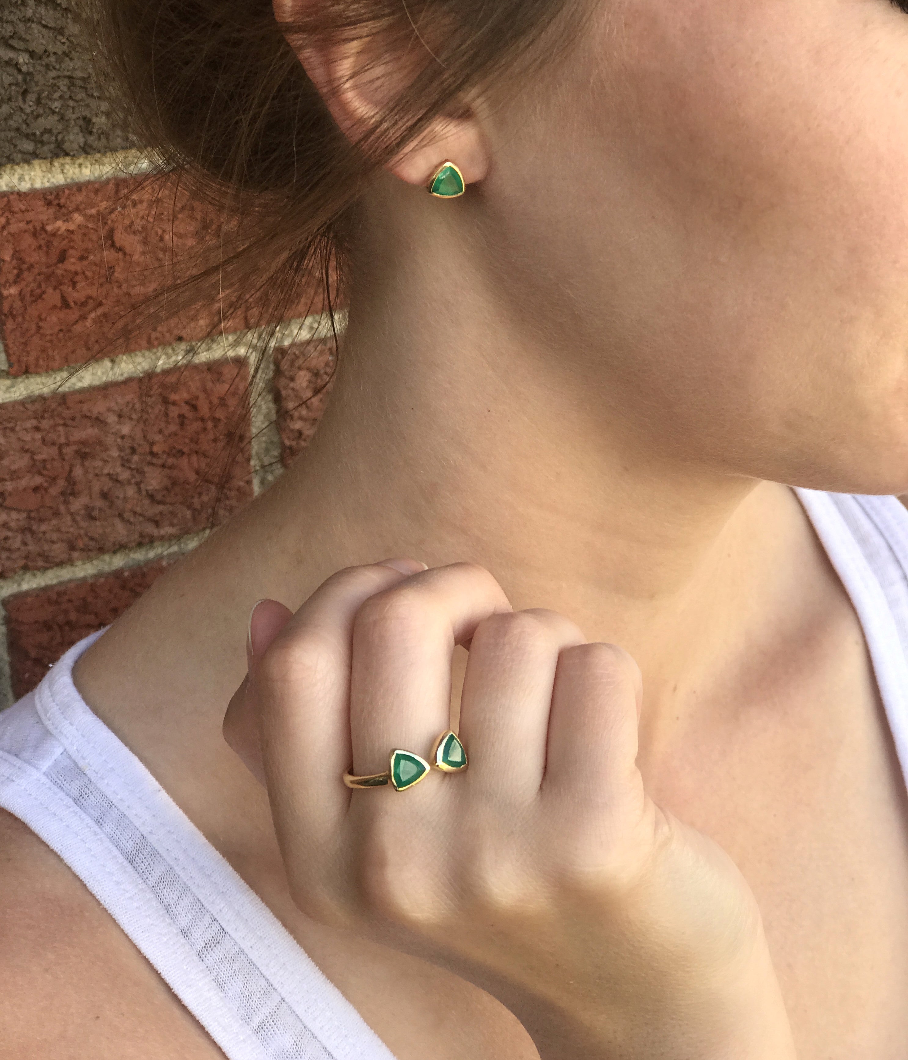 A person wears a set of green onyx triangle stud earrings and a matching green onyx triangle bow tie ring.  Customizable birthstone ring, adjustable triangle bow tie ring, personalized gemstone jewelry, sterling silver triangle ring, gold bow tie ring, rose gold triangle ring, mix-and-match birthstones, unique double triangle ring, adjustable gemstone ring, custom bow tie jewelry, bespoke birthstone ring, chic triangle-cut ring, elegant birthstone ring, unique gemstone gift, customizable stacking ring