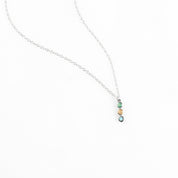 Sterling silver vertical bar necklace with rainbow arrangement of three birthstones: March Aquamarine, October Tourmaline, December Blue Topaz, displayed on a white background. Personalized necklace allows choice of birthstones for a family-inspired jewelry keepsake. Minimalist style perfect for layering with other necklaces or wearing as a meaningful stand-alone piece.