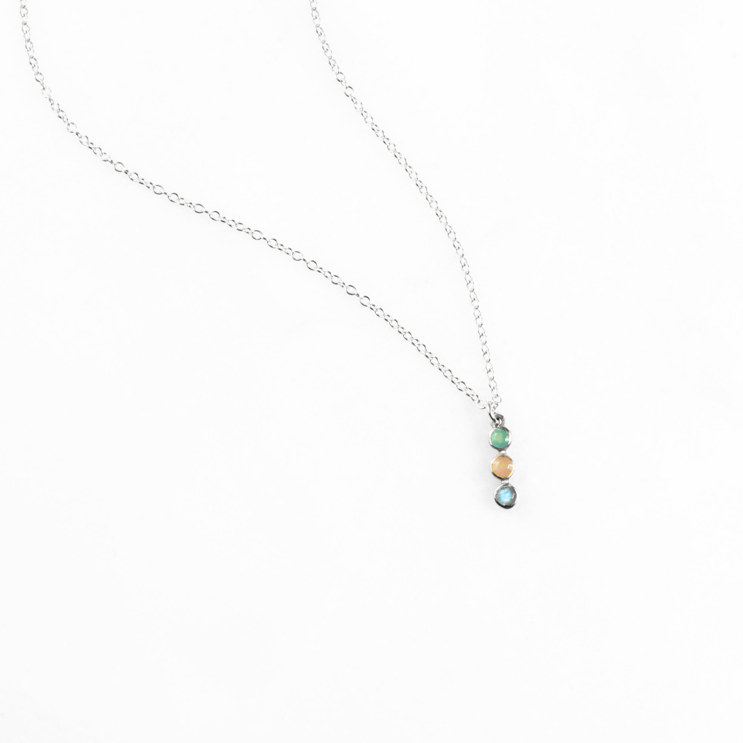 Sterling silver vertical bar necklace with rainbow arrangement of three birthstones: March Aquamarine, October Tourmaline, December Blue Topaz, displayed on a white background. Personalized necklace allows choice of birthstones for a family-inspired jewelry keepsake. Minimalist style perfect for layering with other necklaces or wearing as a meaningful stand-alone piece.